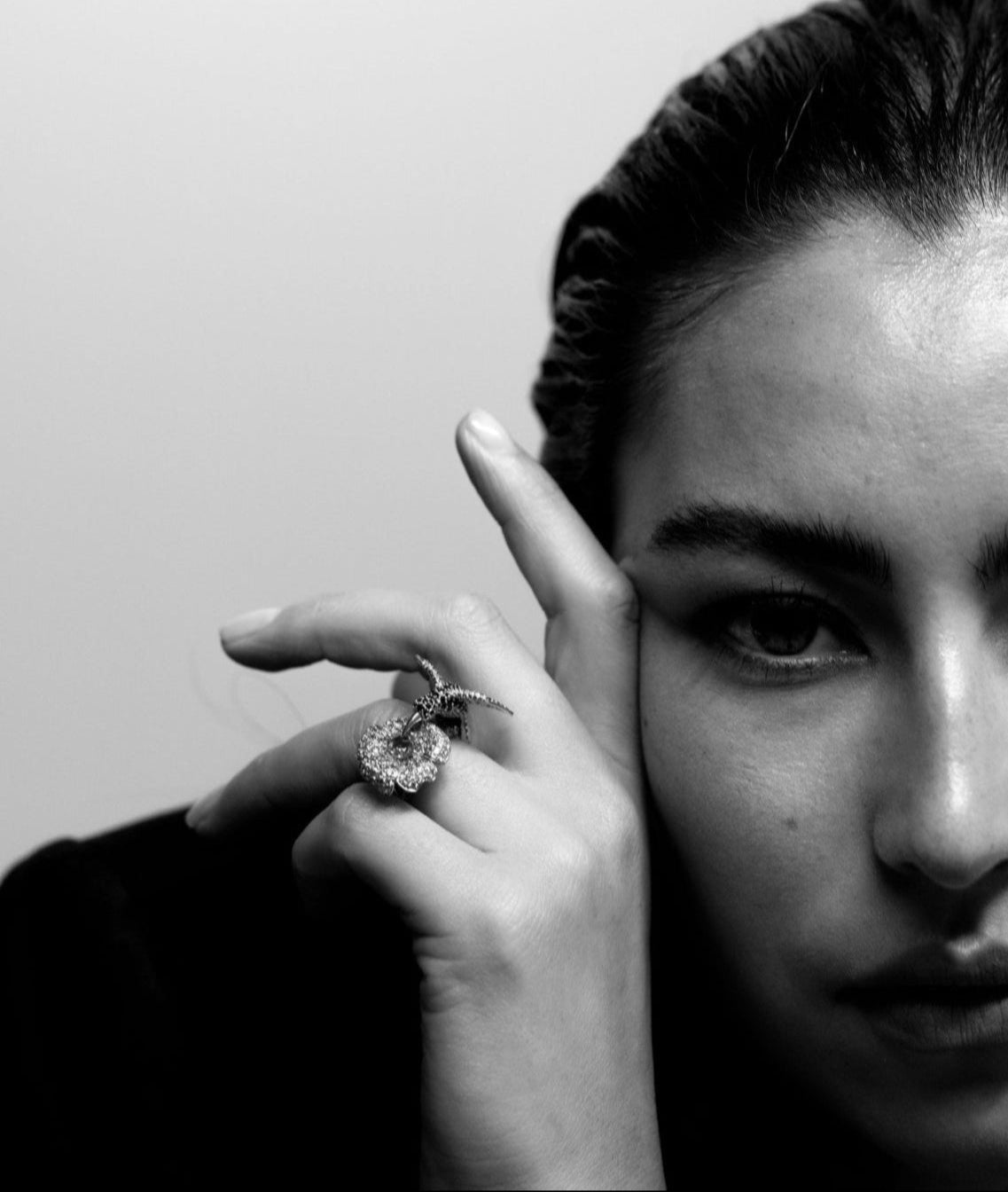Black and white portrait of a person wearing a humming bird ring huon a plain background