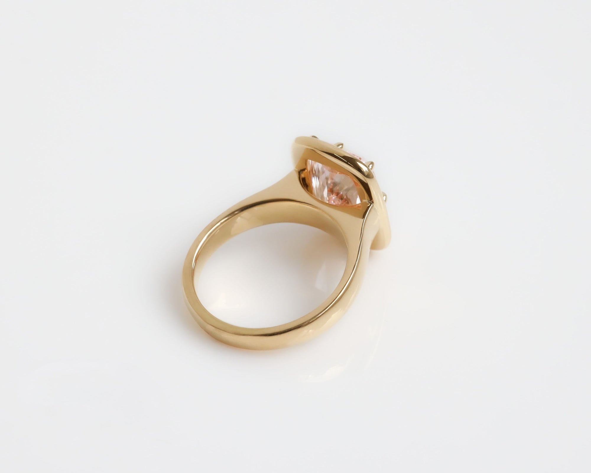 Upward angle of a large pink diamond ring with an 18k yellow gold band on a grey background. 