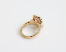 Upward angle of a large pink diamond ring with an 18k yellow gold band on a grey background. 
