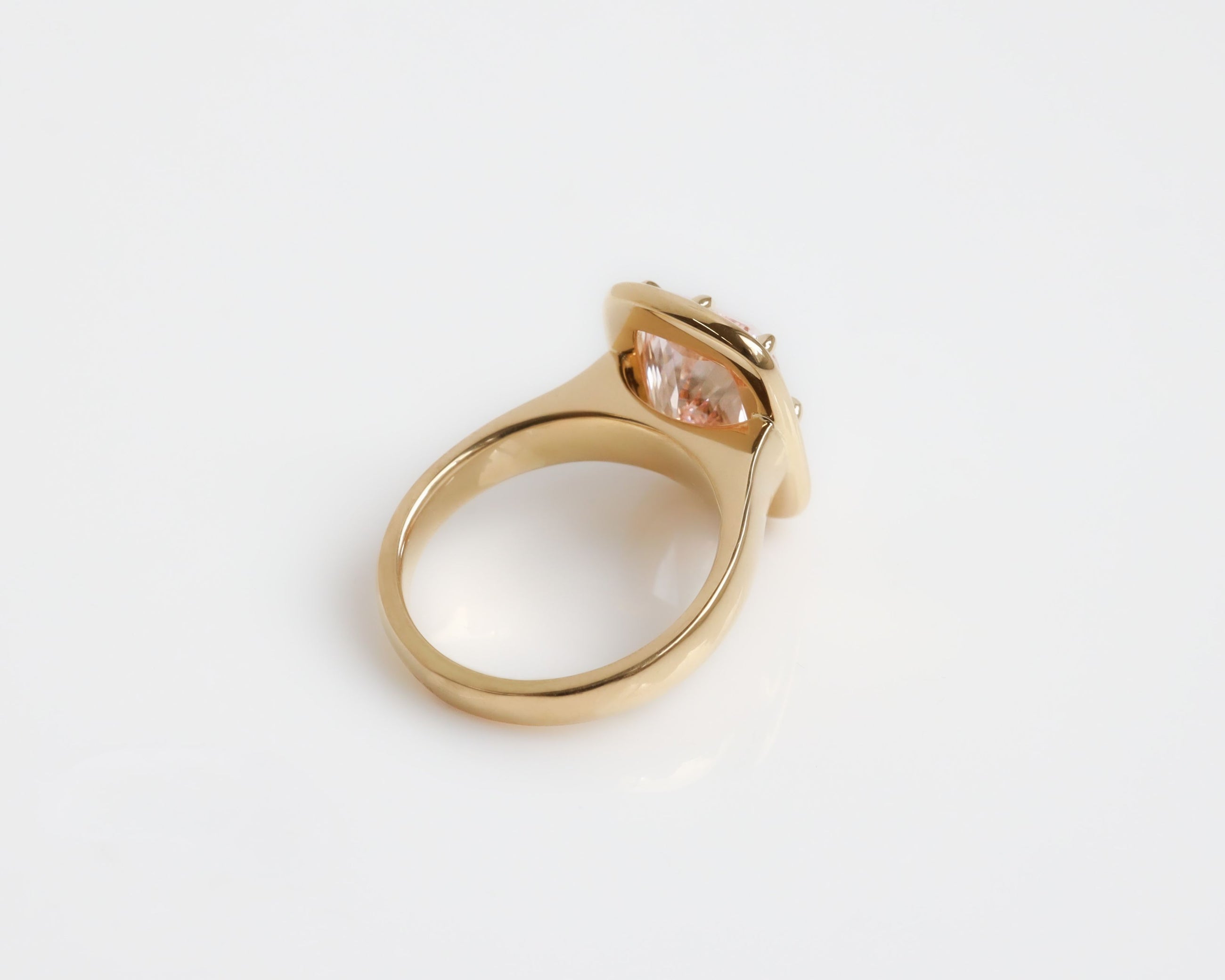 Upward angle of a large pink diamond ring with an 18k yellow gold band on a grey background. 