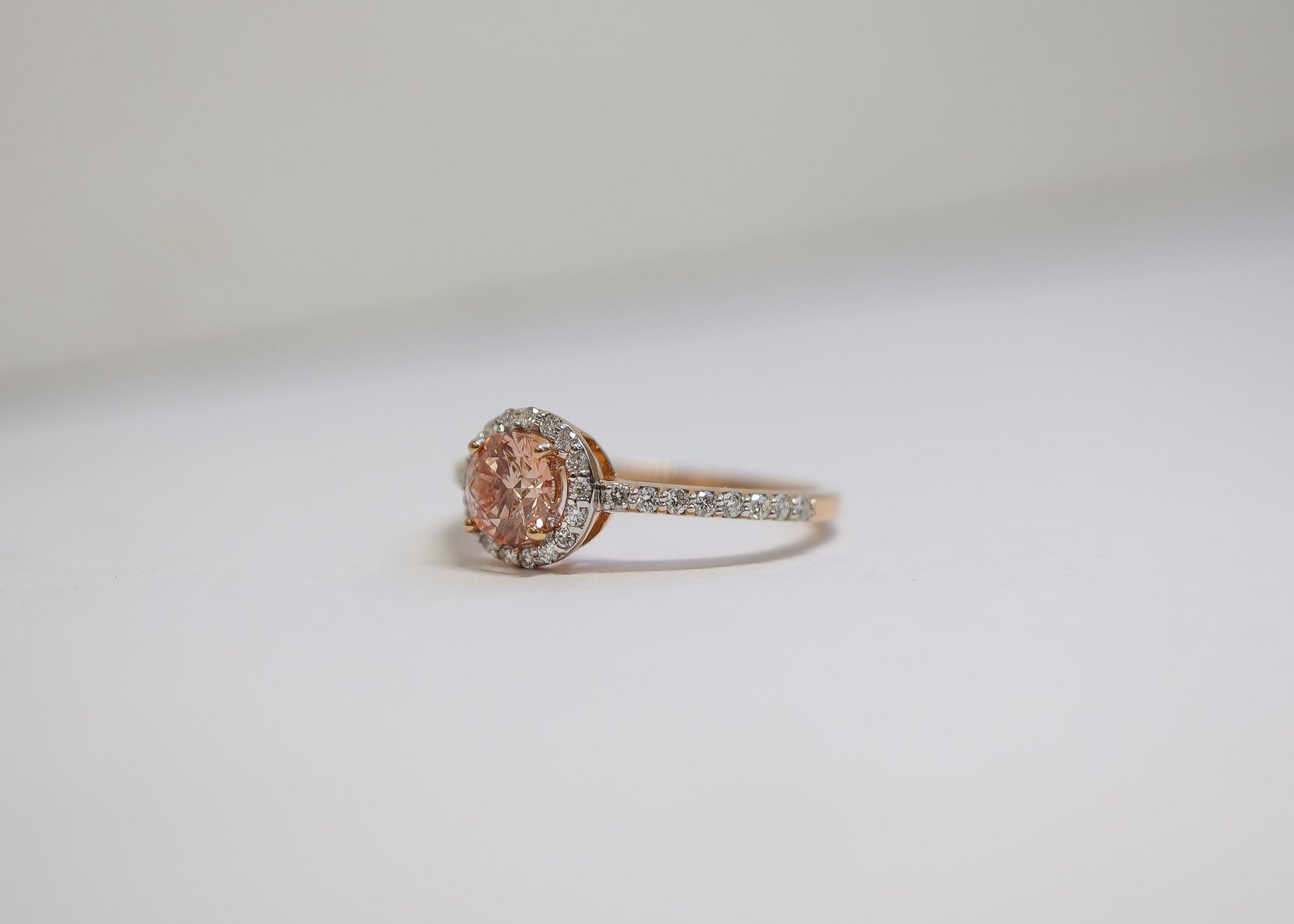 Rose gold ring with a central gemstone and diamond accents on a light gray background