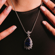 close up of a model wearing A blue tanzanite pendant necklace with a chain, encrusted with diamonds.