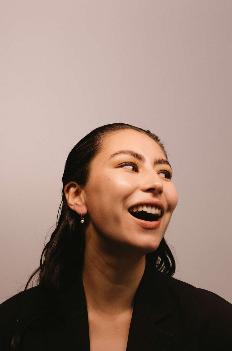 Woman laughing with a neutral background and diamond huggie earrings