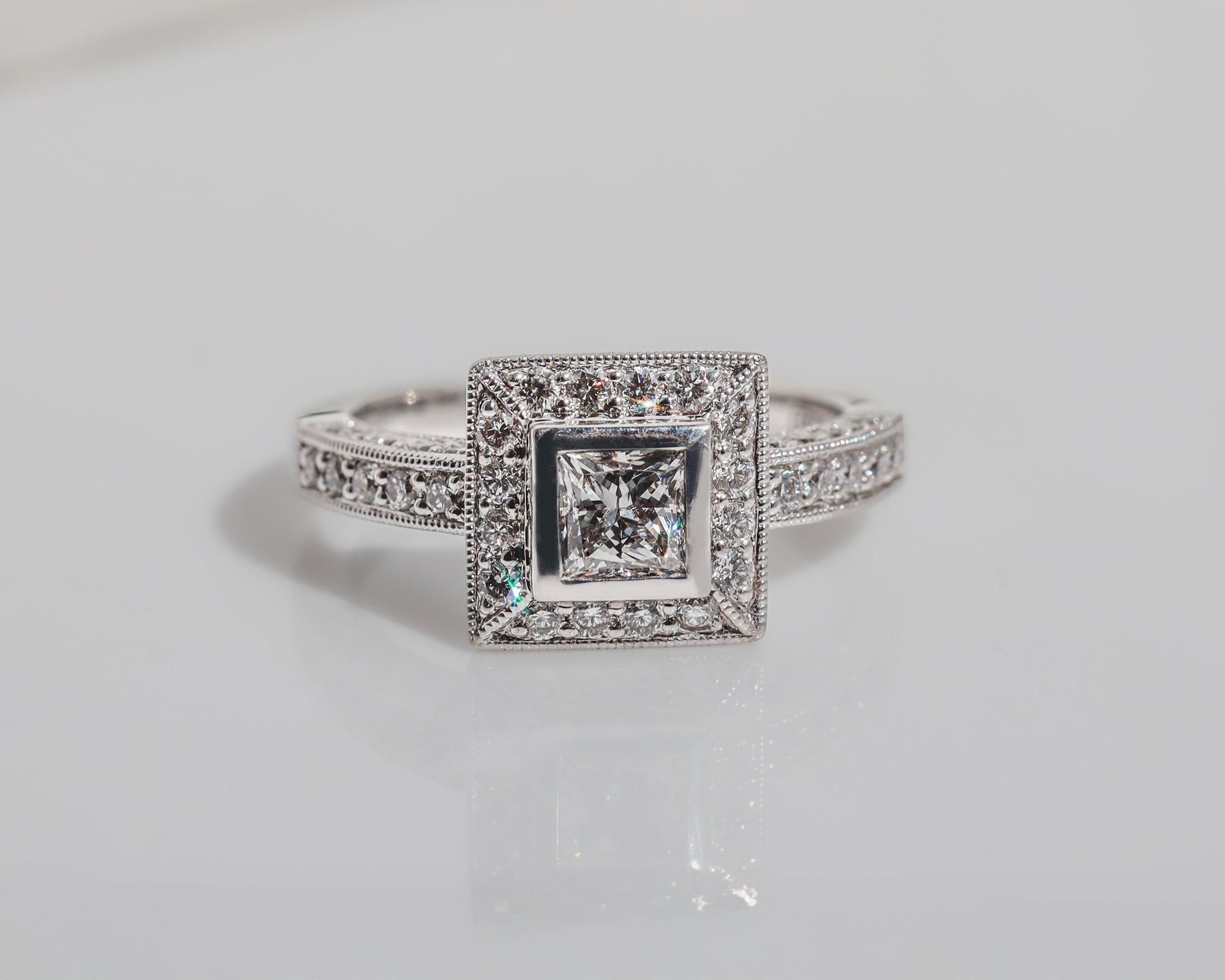 Front view of a diamond engagement ring featuring a halo of diamonds around the centre stone and rows of diamonds along the band.