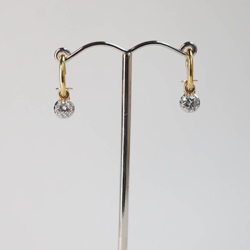 Gold and platinum diamond earrings on a stand against a gray background