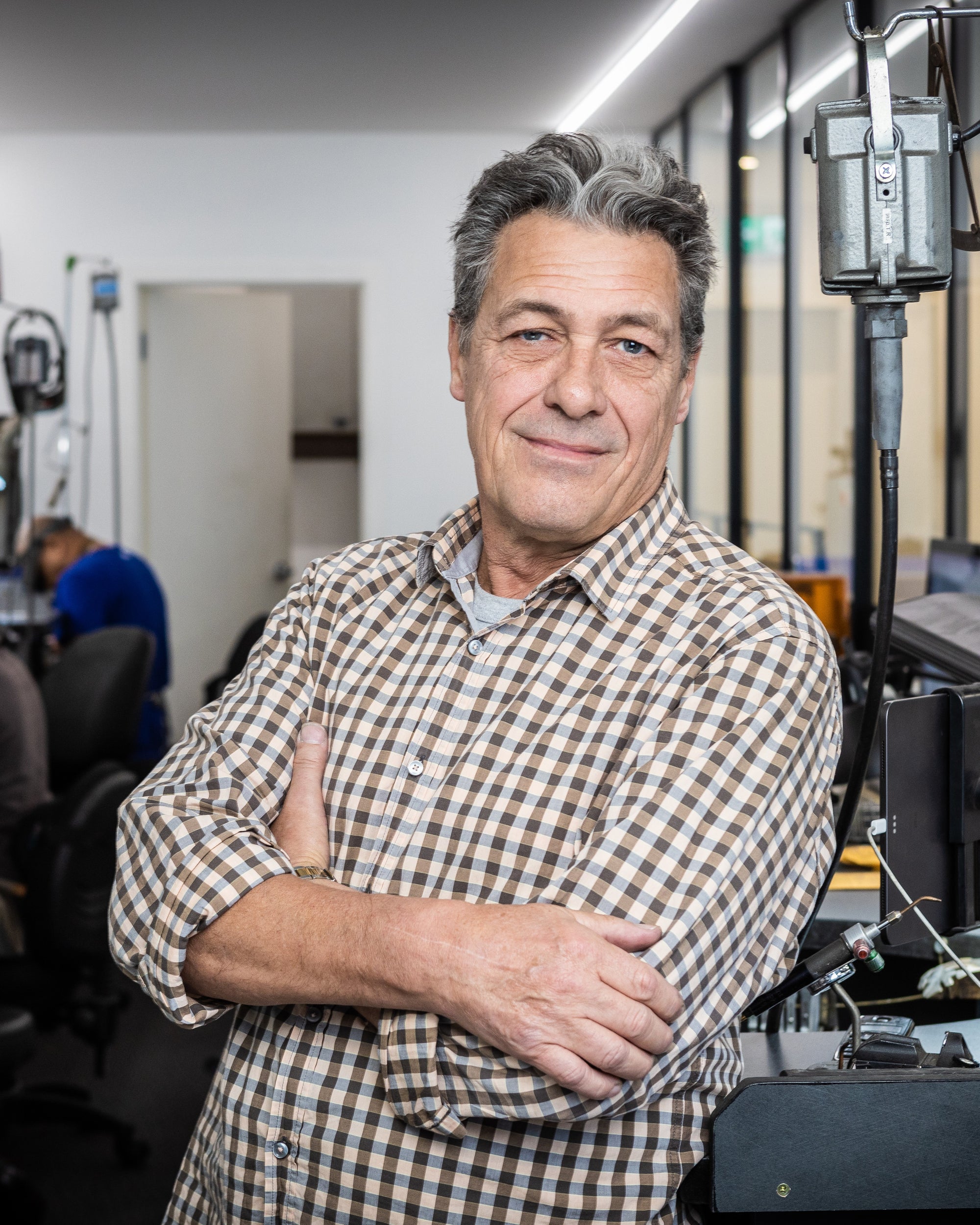 Man wearing a checkered shirt standing in an indoor setting with equipment in the background
