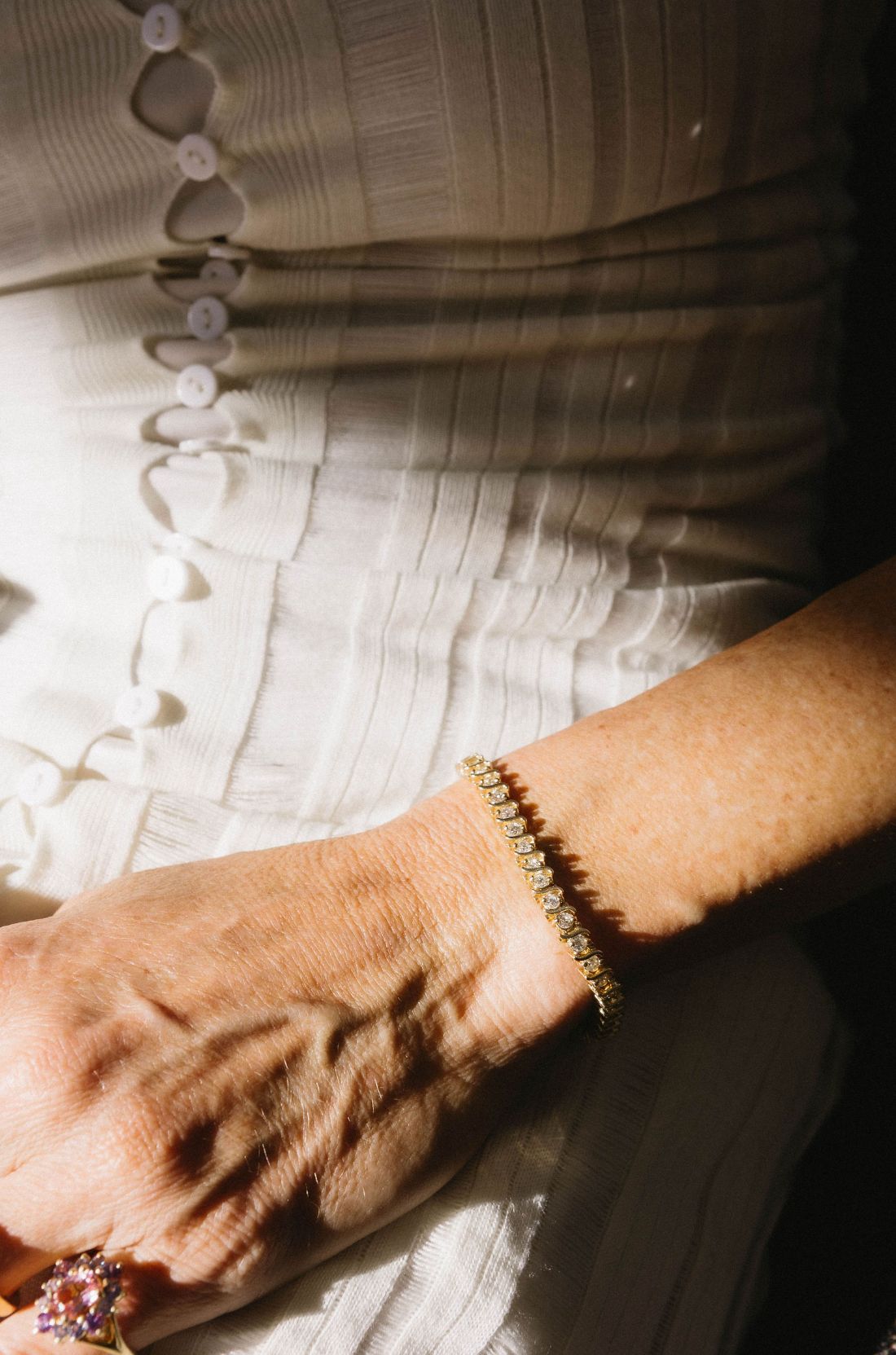 Close-up of a woman's wrist with a 18k yellow gold bracelet, set with natural diamonds all the way around. She also wears a ring in a textured dress.