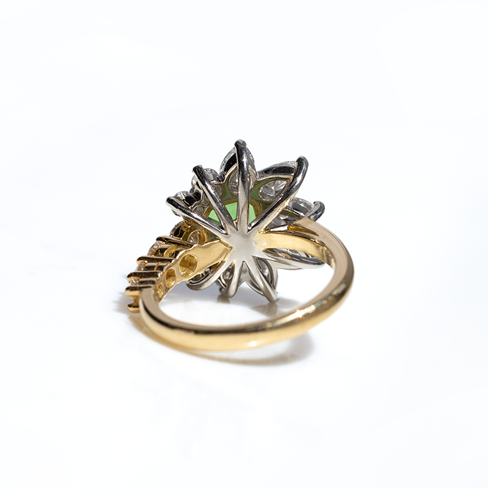The behind of a asymmetric tsavorite and diamond ring with a gold band, featuring a prominent green tsavorite cut in an octagonal shape, flanked by smaller round brilliant cut diamonds.