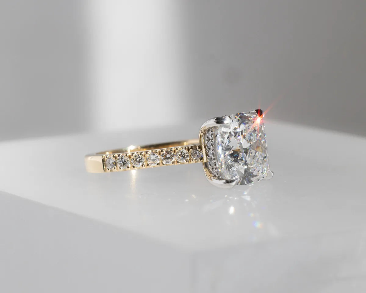 A cushion cut solitaire on a diamond-set gold band