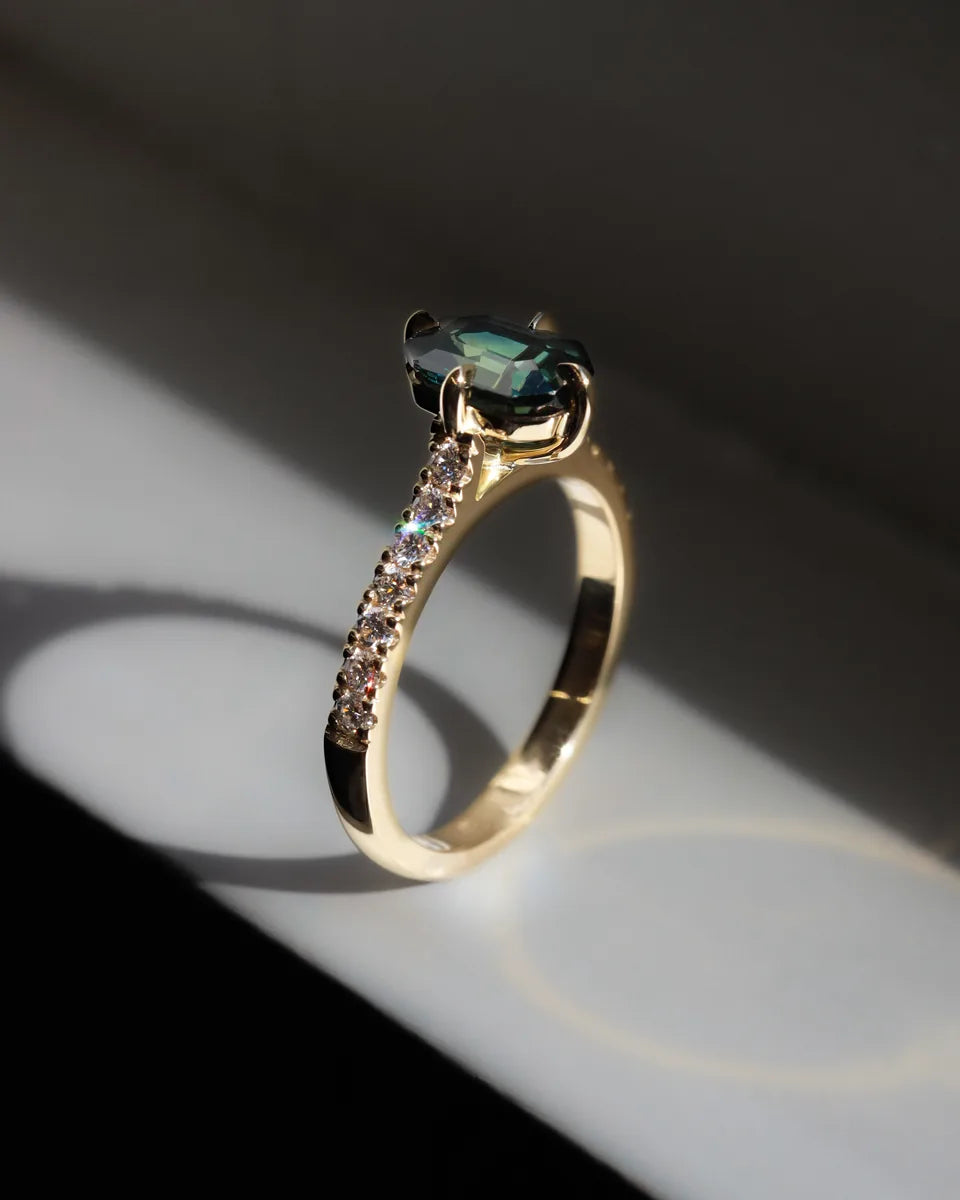 A teal oval gemstone on a diamond-set yellow gold band